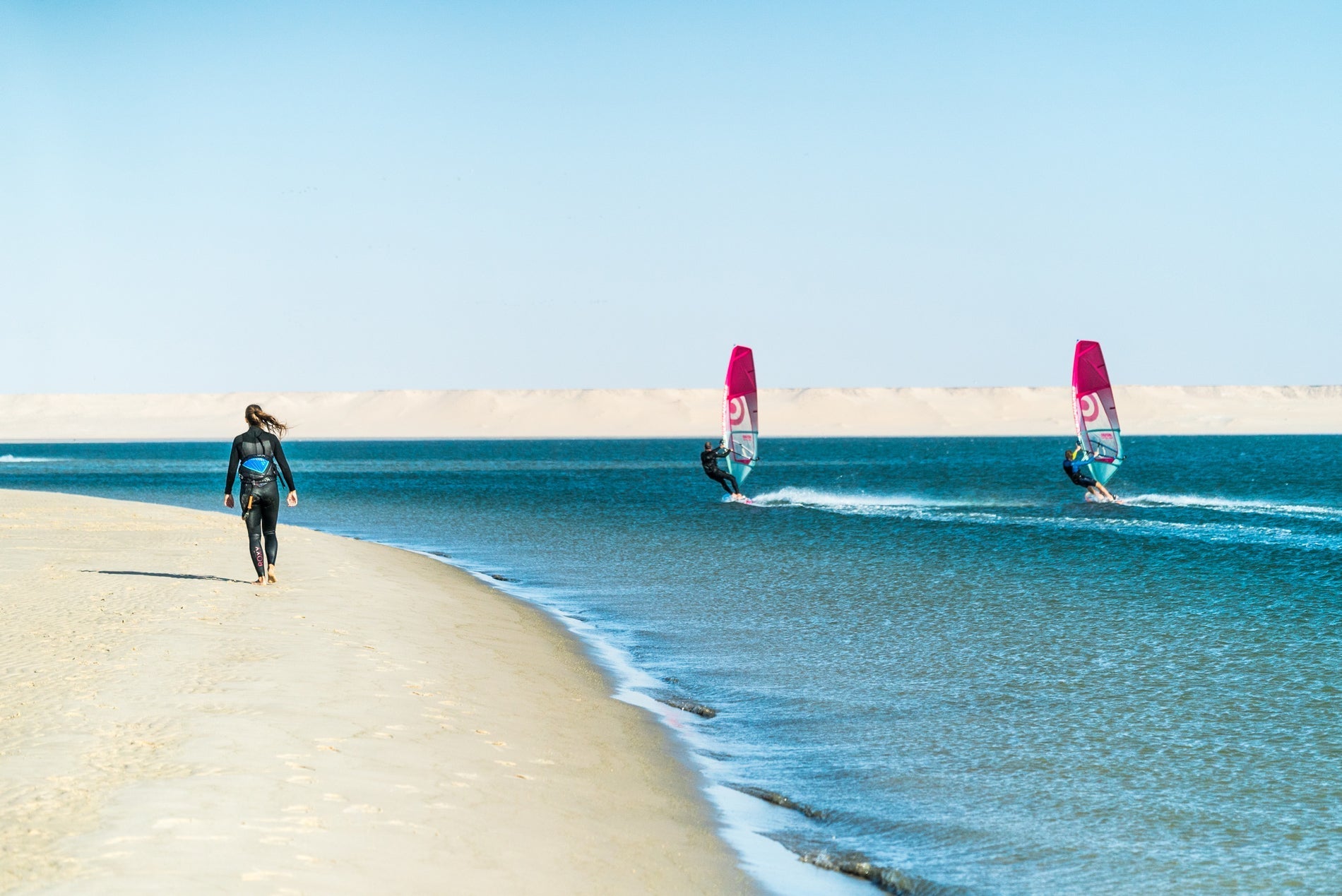 Windsurfers op vlak water langs het strand