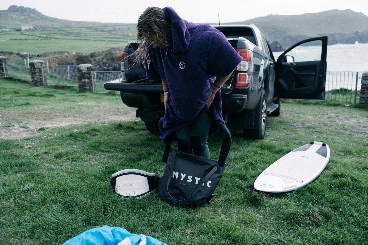 Surfer kleedt zich om in een poncho naast de Mystic Happy Hour Wetsuit Changing Bucket