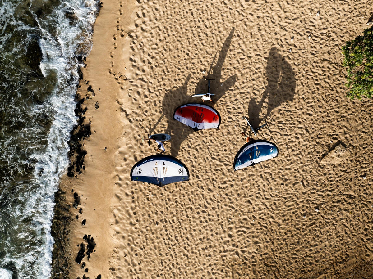 Drie Naish ADX wings in de kleurstellingen naast elkaar op het strand