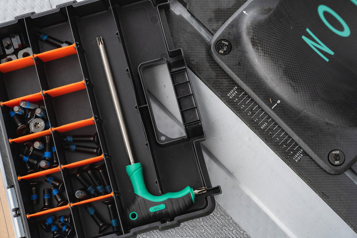 Geopende North Sonar Session Saver Box met titanium schroeven, reserveonderdelen en T-sleutel naast een foilboard