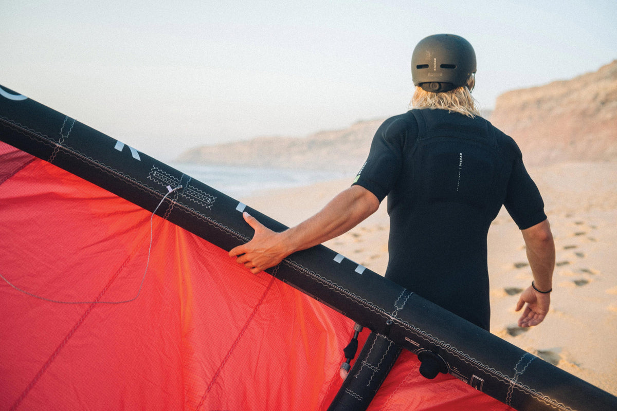 Rider in Mystic Impact Shorty met helm loopt met een kite over het strand