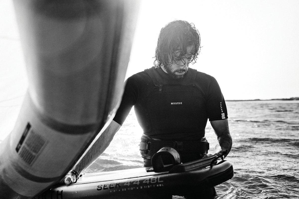 Rider met Mystic Impact Shorty en trapeze in het water naast een foilboard