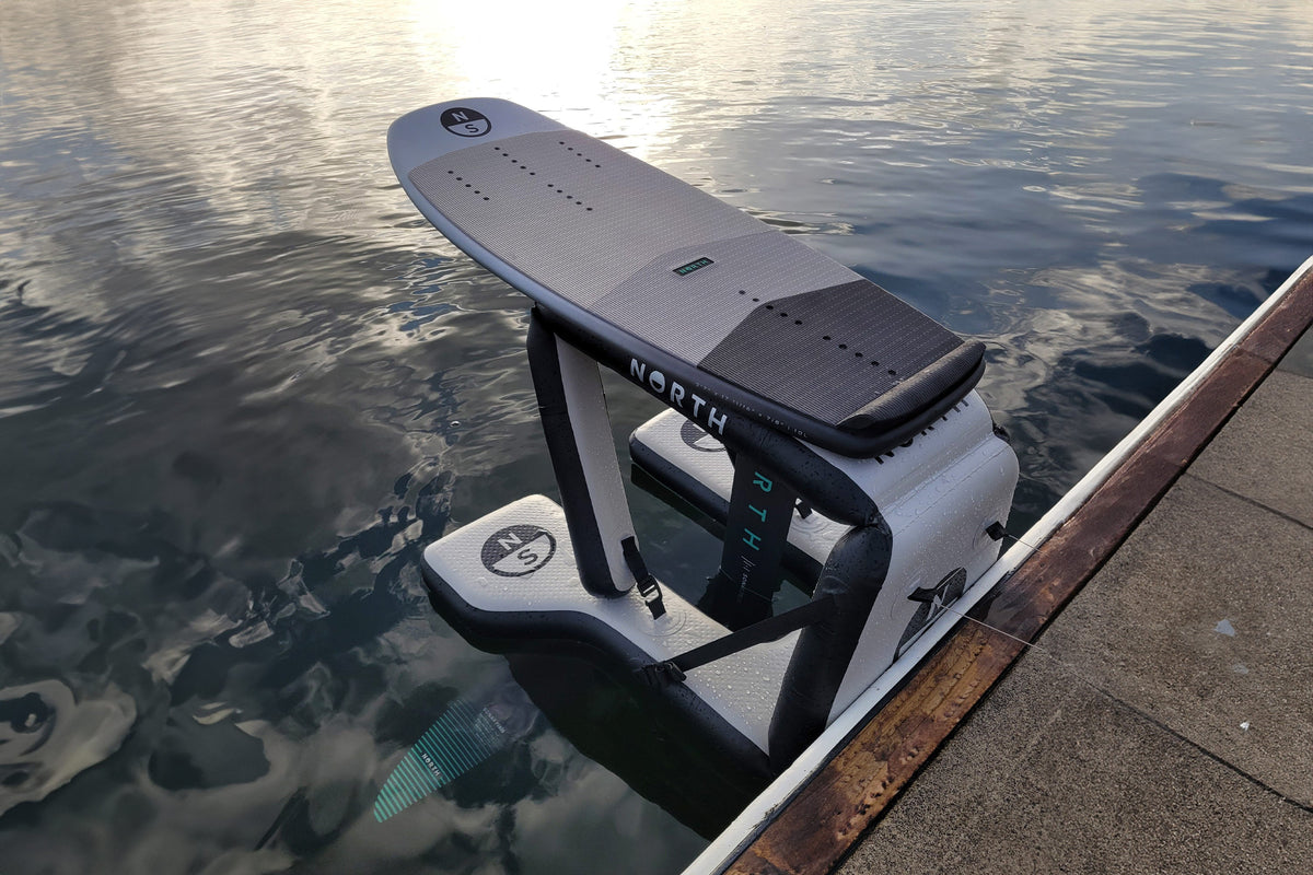 North Dockstarter opblaasbaar launch pad in het water langs een steiger, met een North foilboard erop klaar voor een dockstart
