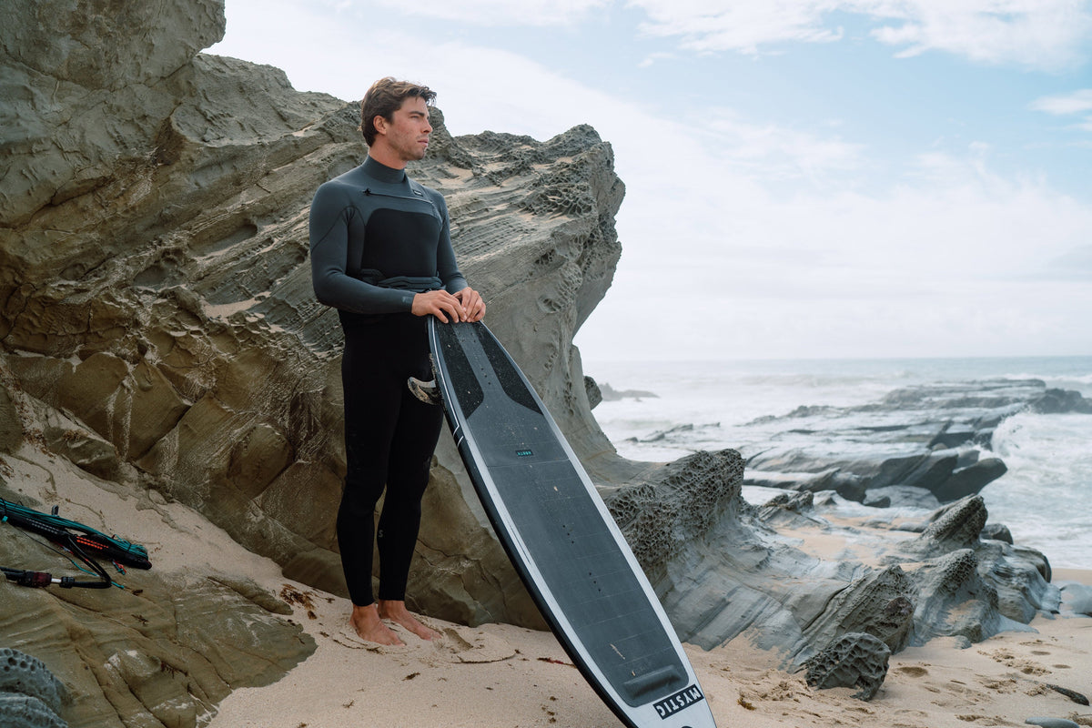 Surfer in een Mystic Motion Fullsuit 3/2mm Fzip op het strand
