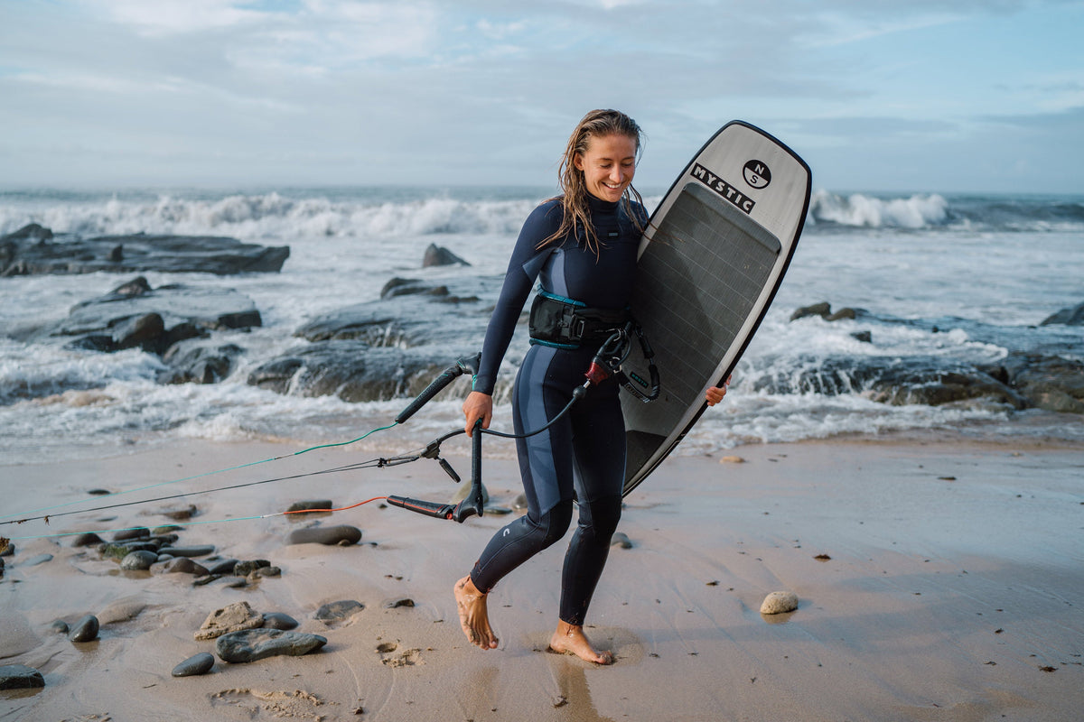 Kitesurfster in een Mystic Haven Fullsuit loopt met haar board over het strand