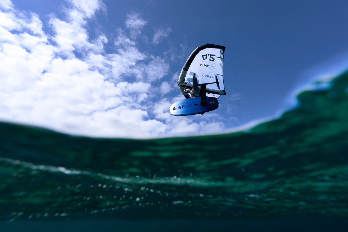 Wingfoiler zweeft met de North Seek Foil Board 2025 in Pacific Blue boven het water, gefotografeerd vanaf wateroppervlak