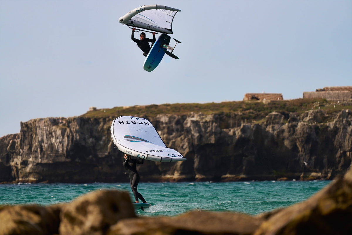 Sprong met de North Seek Foil Board 2025 voor een rotskust, met een tweede wingfoiler op het water
