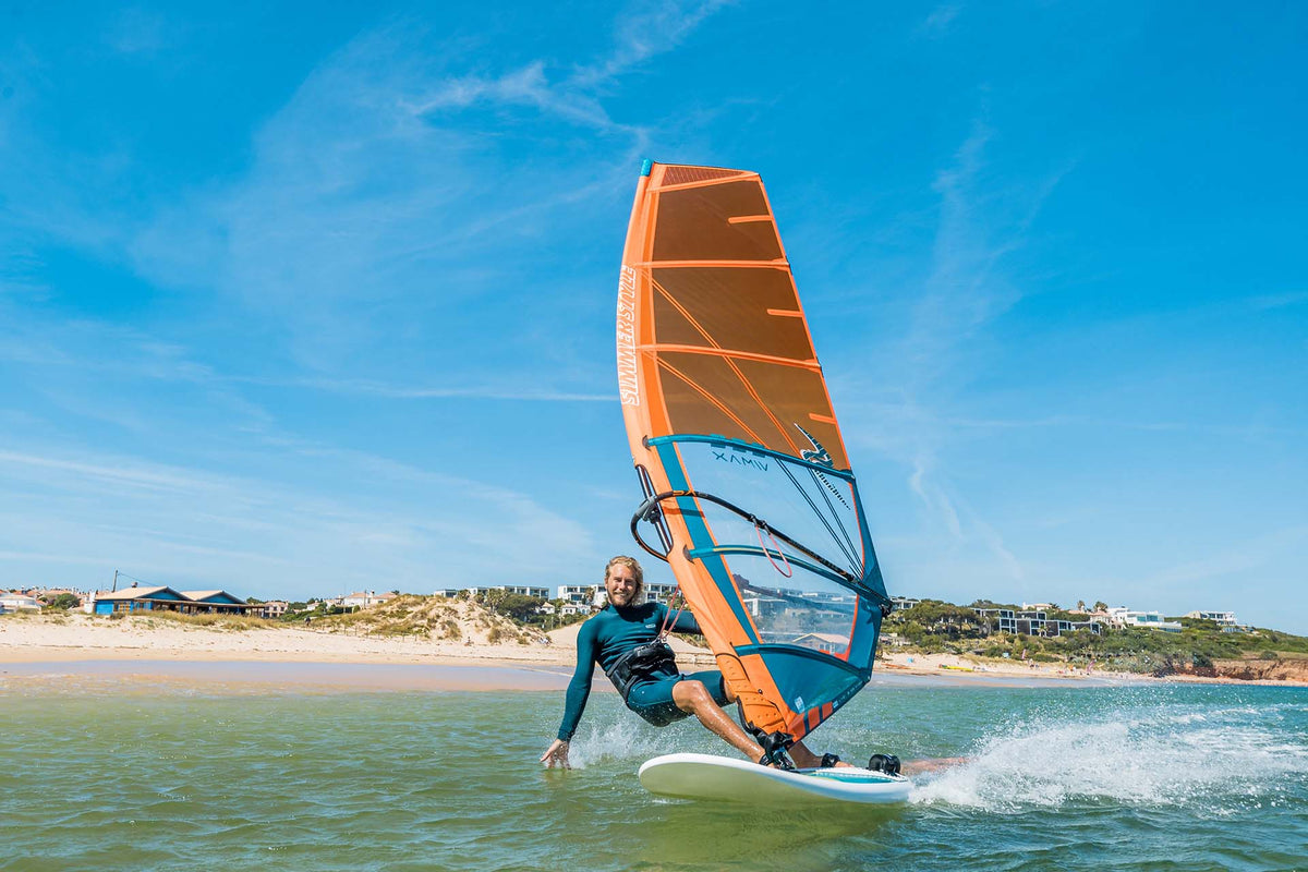 Windsurfer vaart met de Simmer Style Enduro 2024 in oranje langs het strand