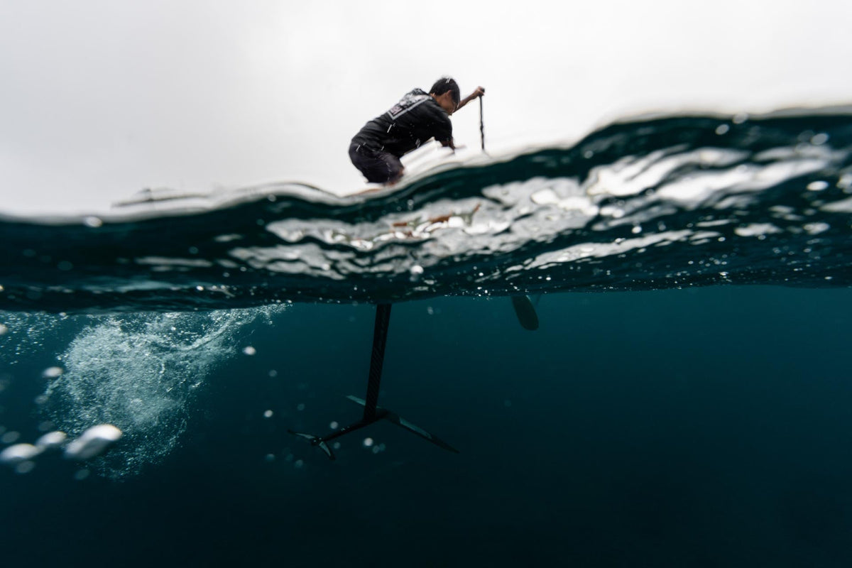 Sup-foilen met de Naish SHA-foil bij Maui, half onder water gefotografeerd: rider met peddel boven water, mast en frontwing eronder