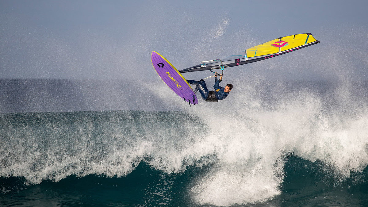 Duotone Ultra Grip (Quad) SLS windsurfboard in de lucht boven een brekende golf