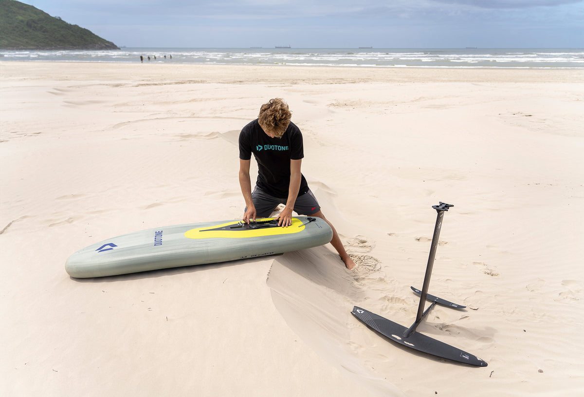 Wingfoiler maakt zijn board klaar op het strand, met de Duotone Free-foil in het zand ernaast