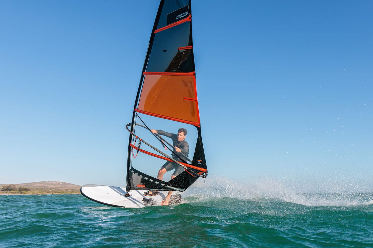 Windsurfer gijpt op de witte RRD Firestorm LTE Y28 met spray onder een strakblauwe lucht