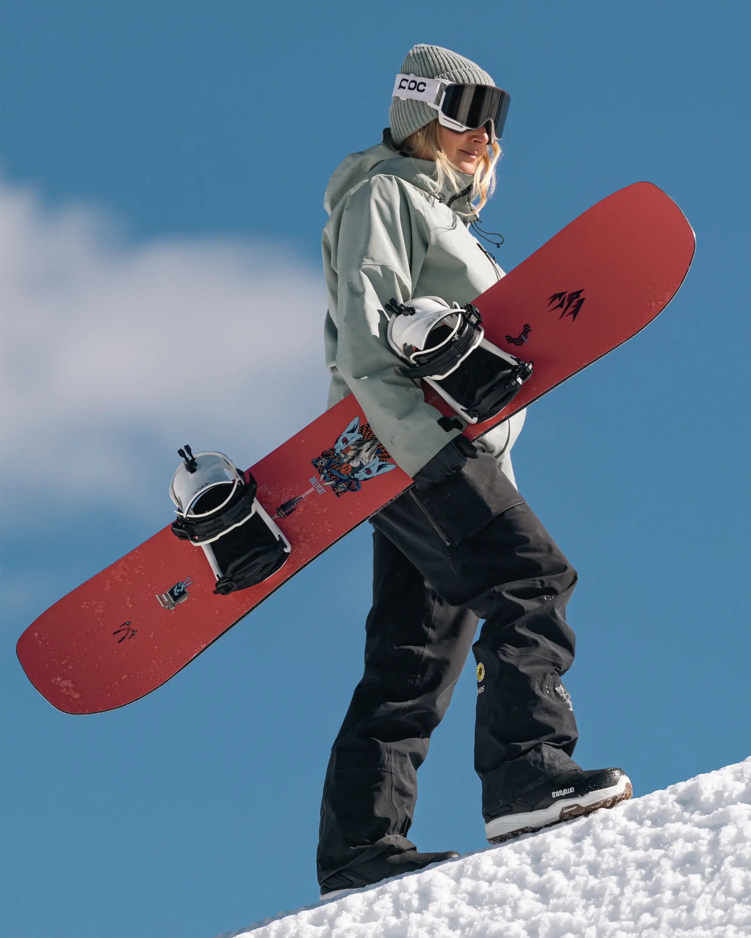 Jones Women's Rally Cat, rider met het board in de hand in de sneeuw