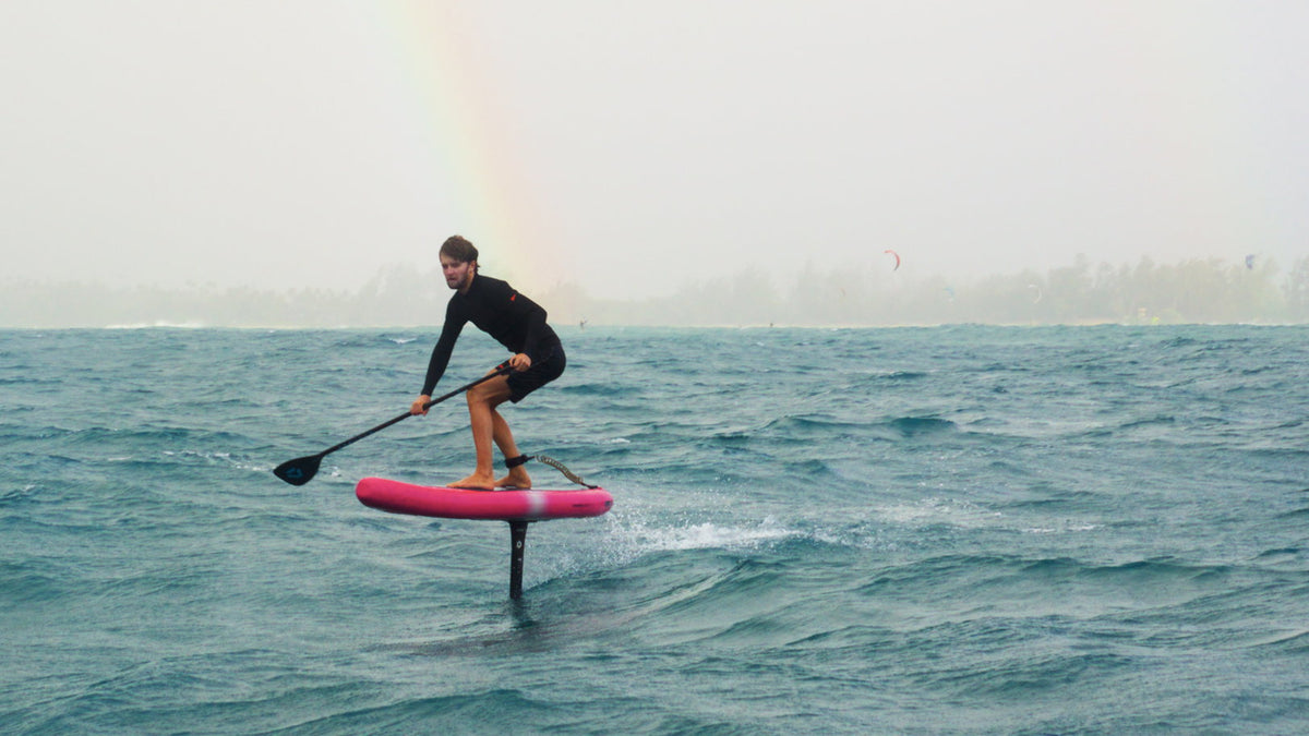 Foilen met peddel op de Duotone Downwinder Air met een regenboog op de achtergrond