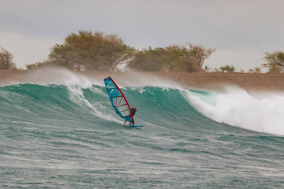 Windsurfer rijdt een golf met de Simmer Style Evoq 2025 Deep Red/Blue