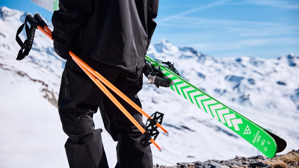 Black Crows Meta Poles oranje, skiër draagt ski en stokken over een besneeuwde bergkam