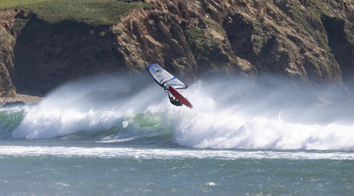 Windsurfer springt met het North Wave GEN3-zeil boven een brekende golf voor de kliffen