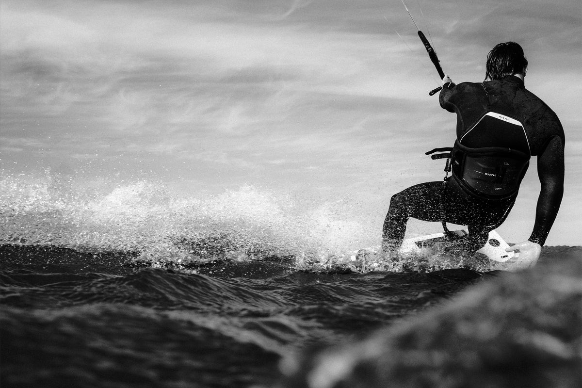 Kitesurfer in de Mystic Majestic Fullsuit met opspattend water, zwart-wit